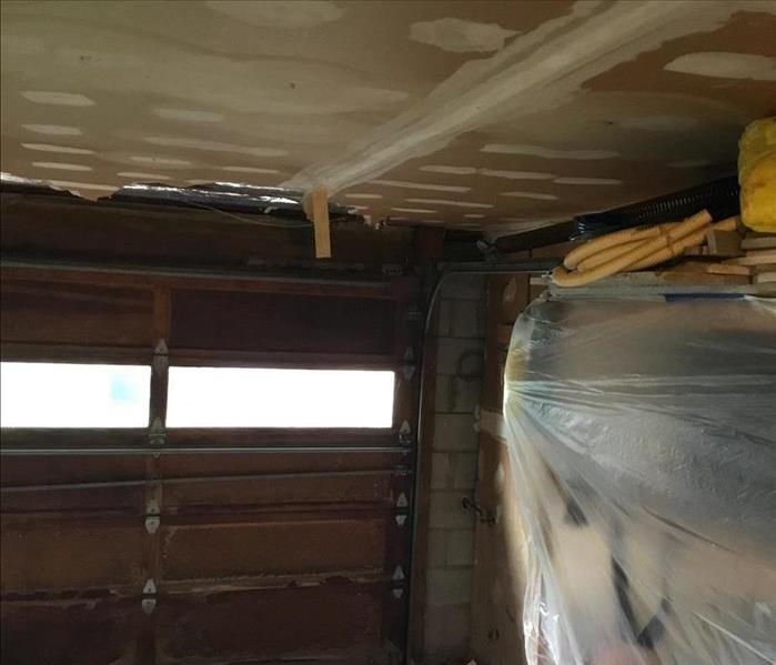 Damaged interior look of garage door and unfinished sheetrock ceiling, and plastic sheeting to protect the items on the shelv